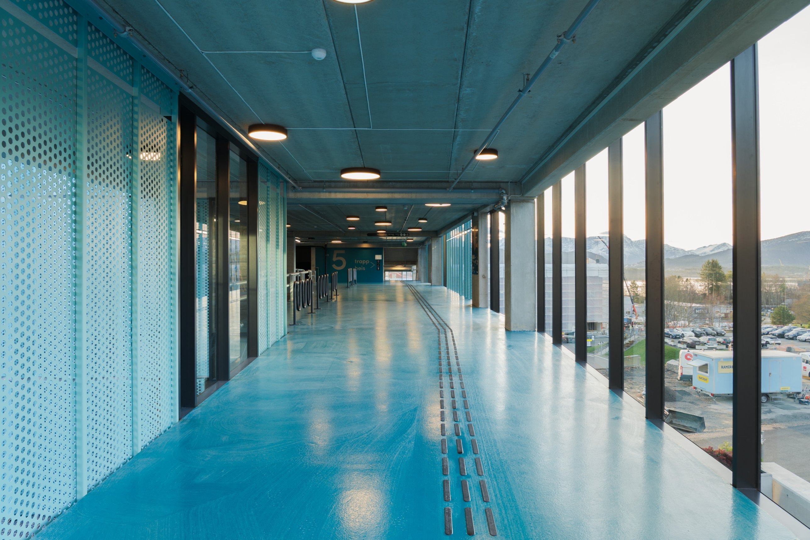 Glass-walled pedestrian walkway with blue floor and mountain view