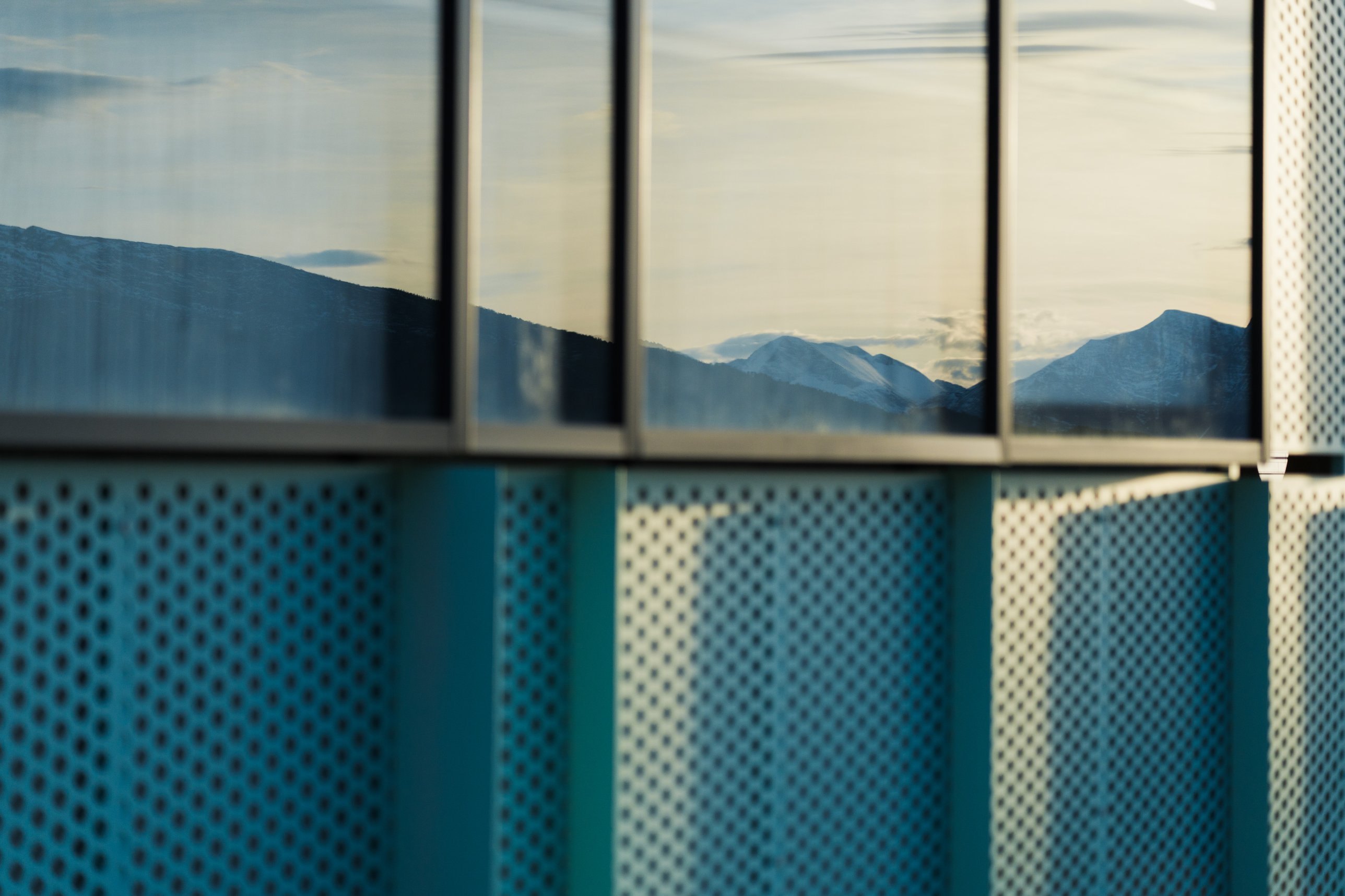 Mountains reflected in windows above perforated facade panels